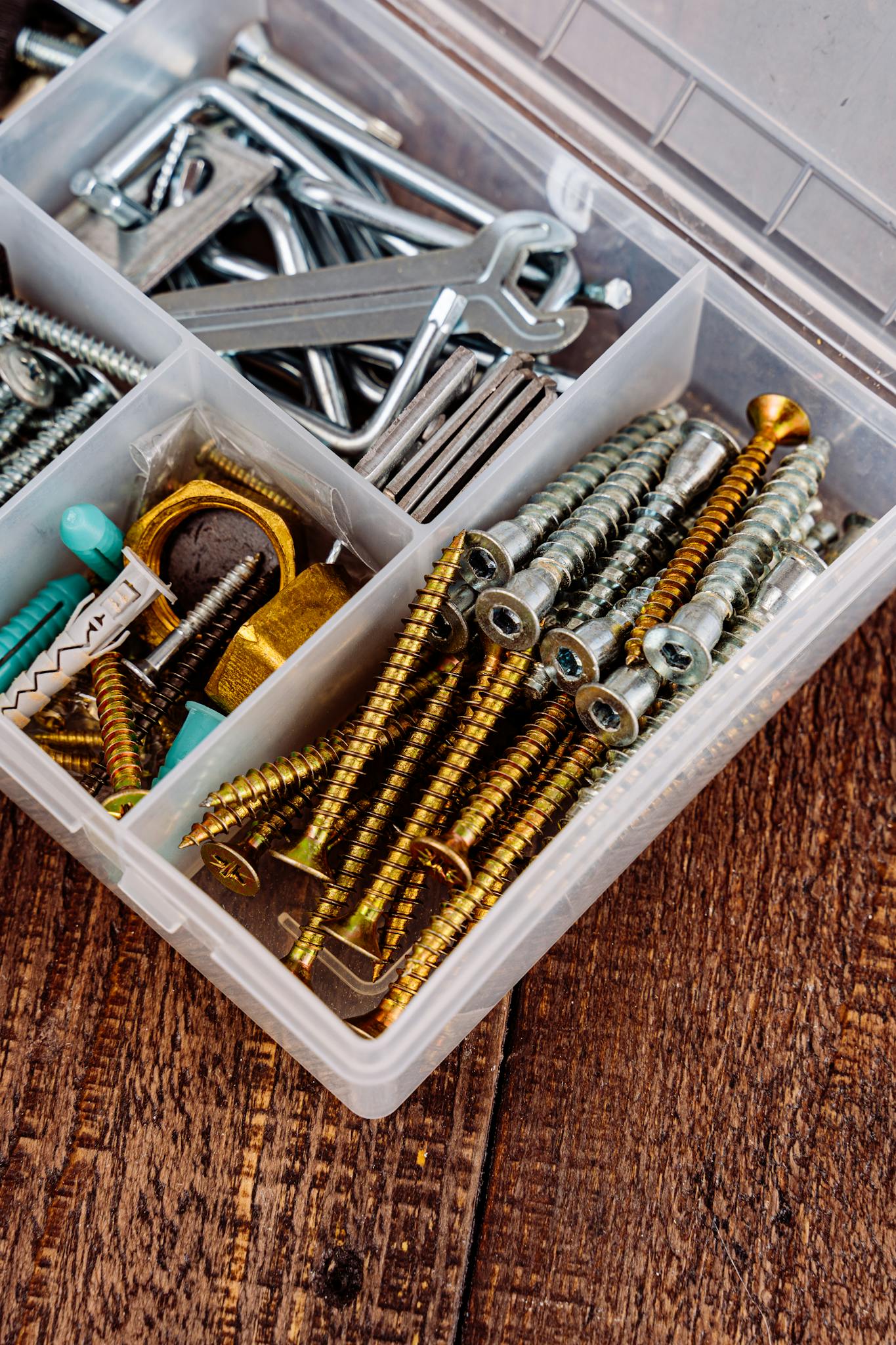 Close-up view of a toolbox containing assorted screws, wrenches, and tools on a wooden surface.